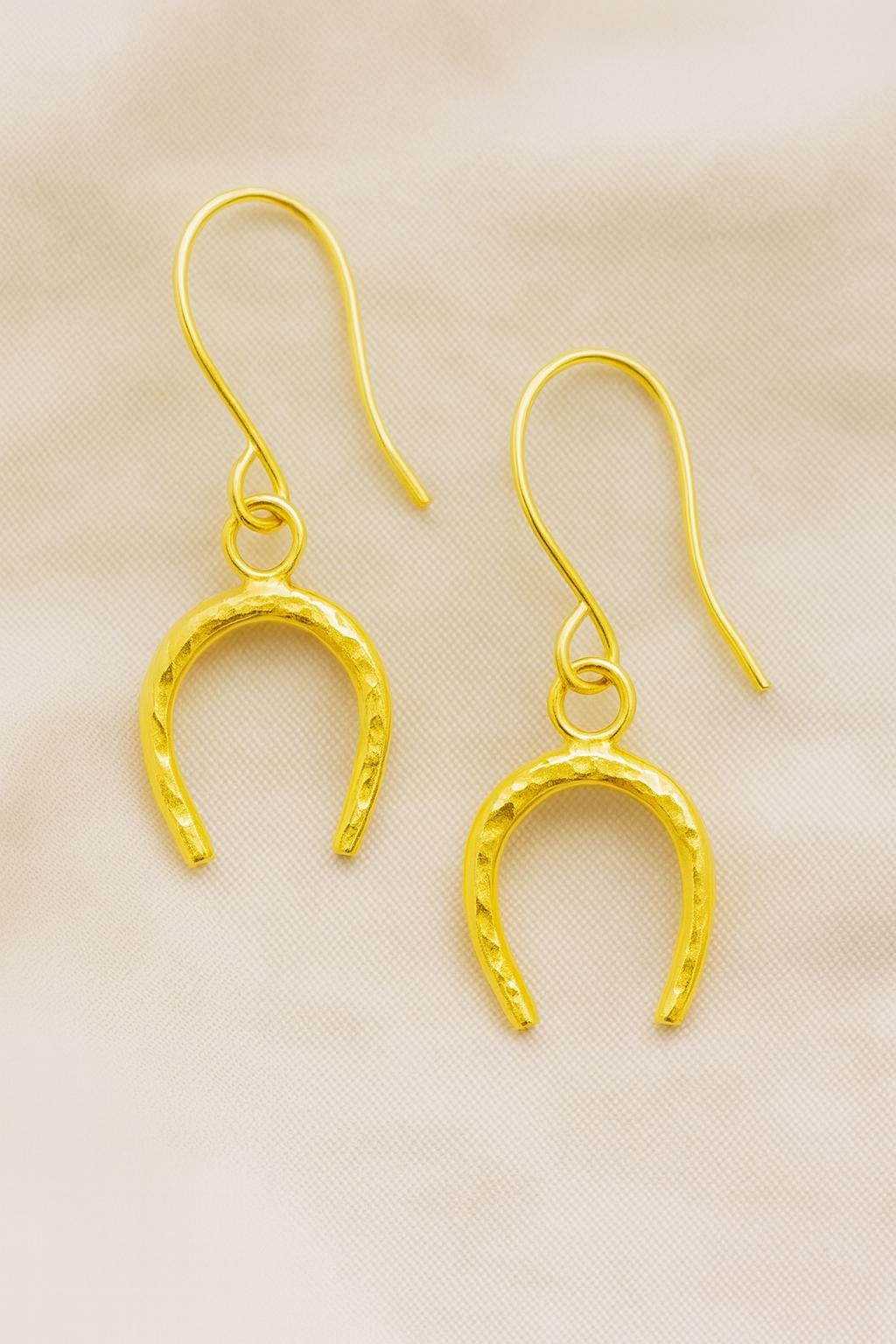 Gold horseshoe-shaped earrings on a beige fabric background