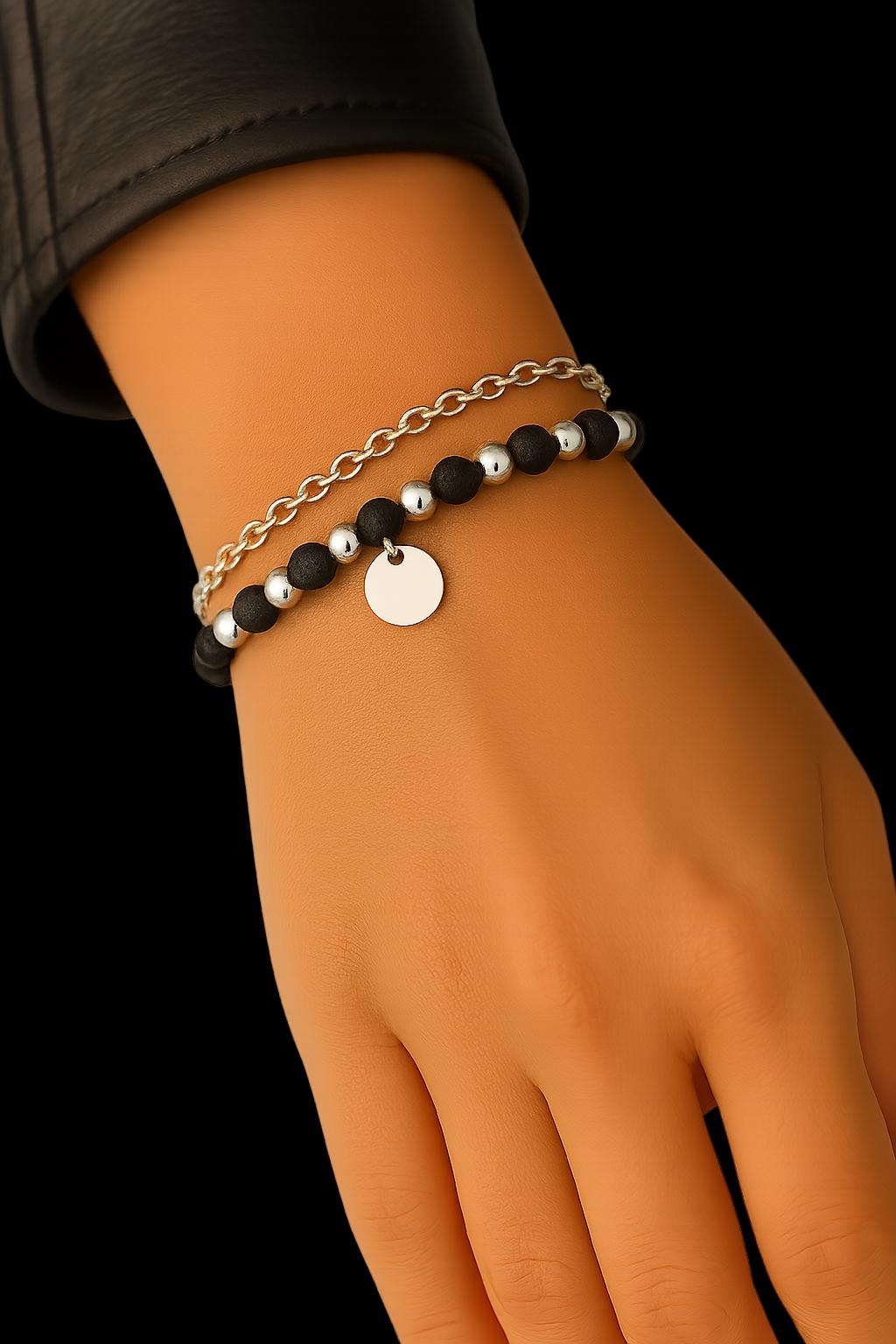 Hand wearing a black beaded bracelet with a silver tag on a black background