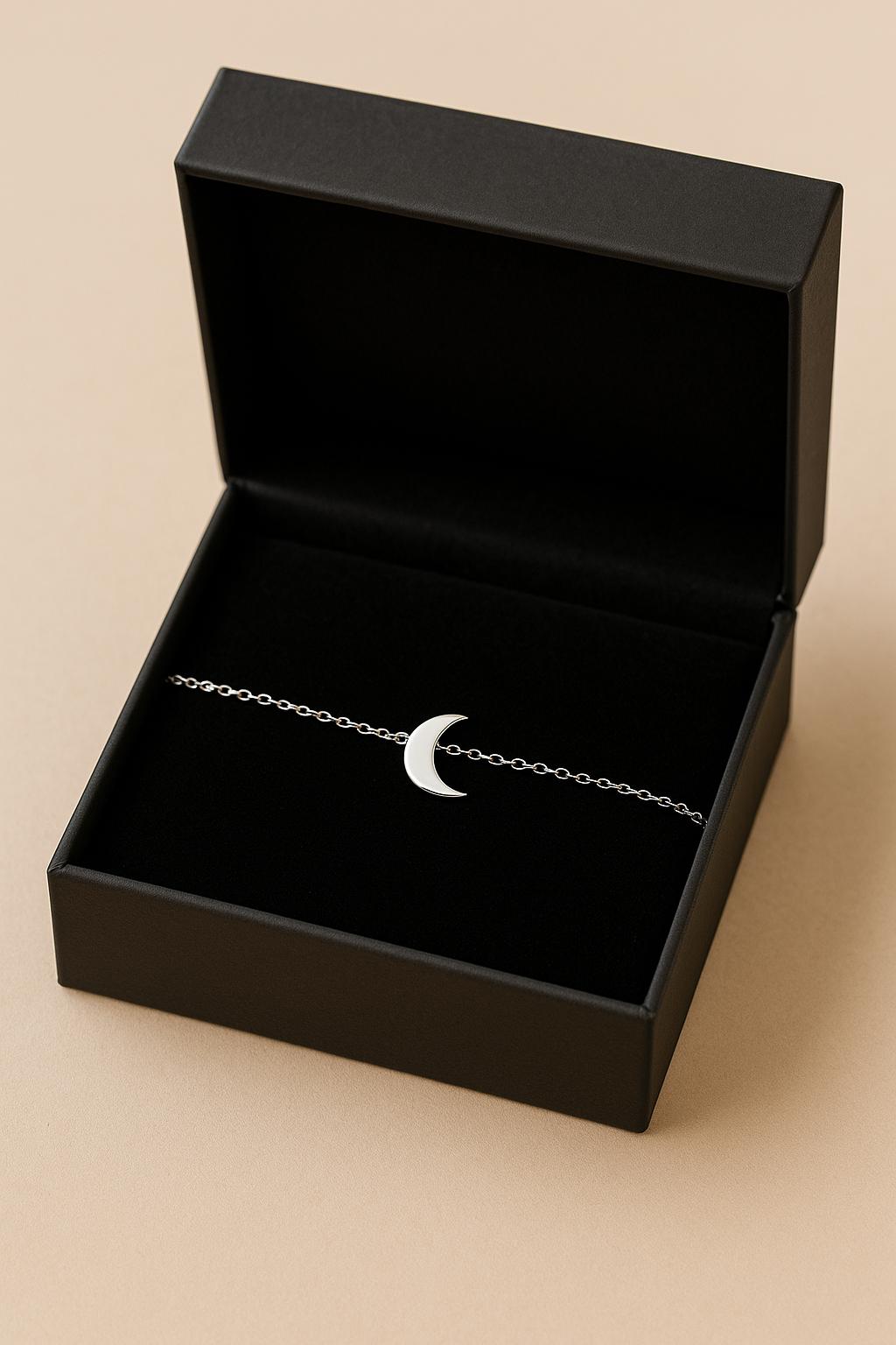 Black jewelry box with a silver bracelet featuring a moon charm on a beige background