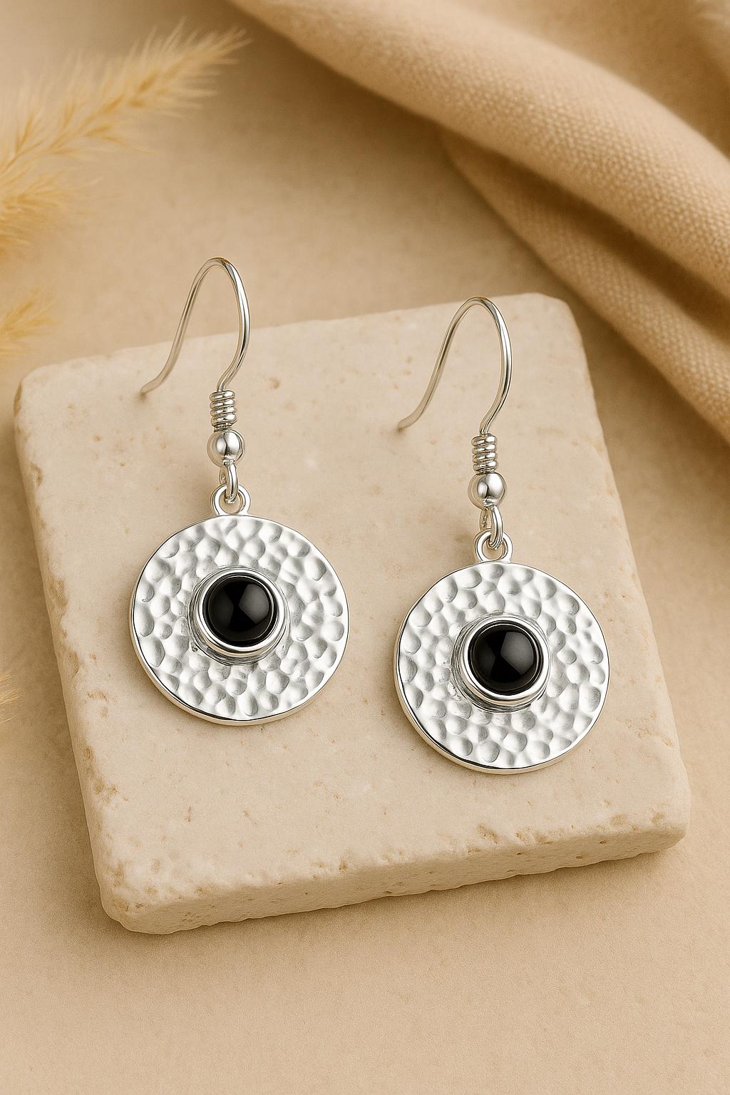 Silver earrings with black onyx gemstone stones on a beige stone surface