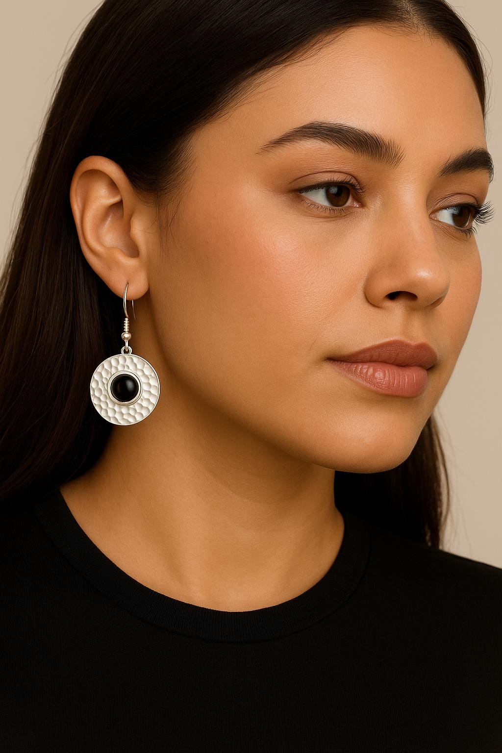 Close-up of a woman wearing a silver earring with a black gemstone on a neutral background