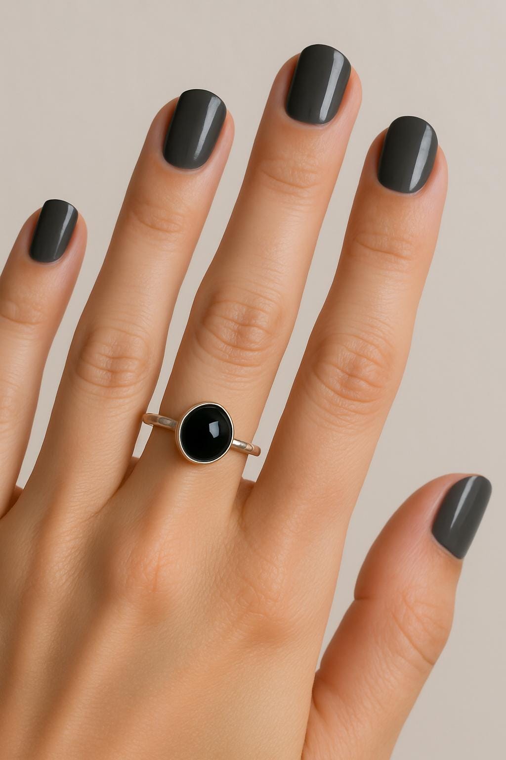 Hand wearing a silver ring with a black gemstone against a neutral background