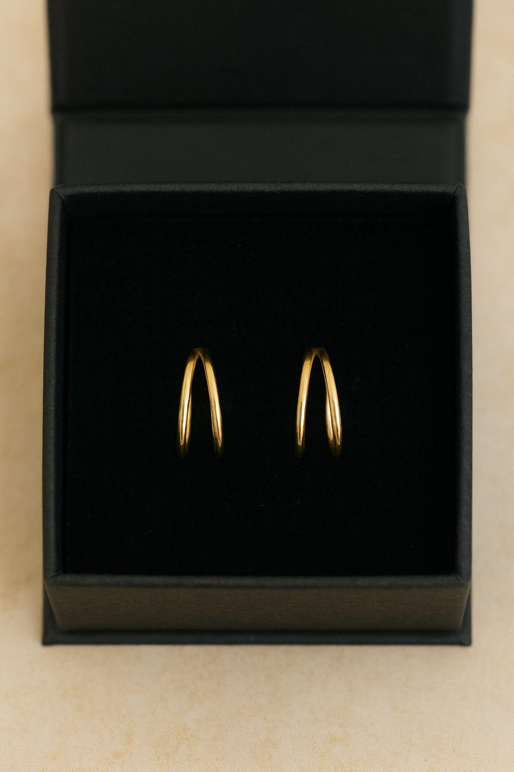 Gold hoop earrings in a black jewelry box on a beige background