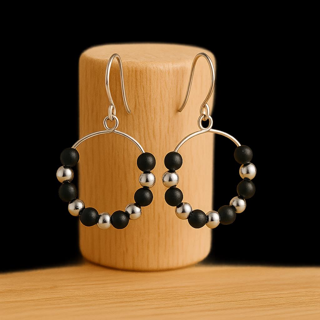 Hoop earrings with black and silver beads on a wooden stand against a black background