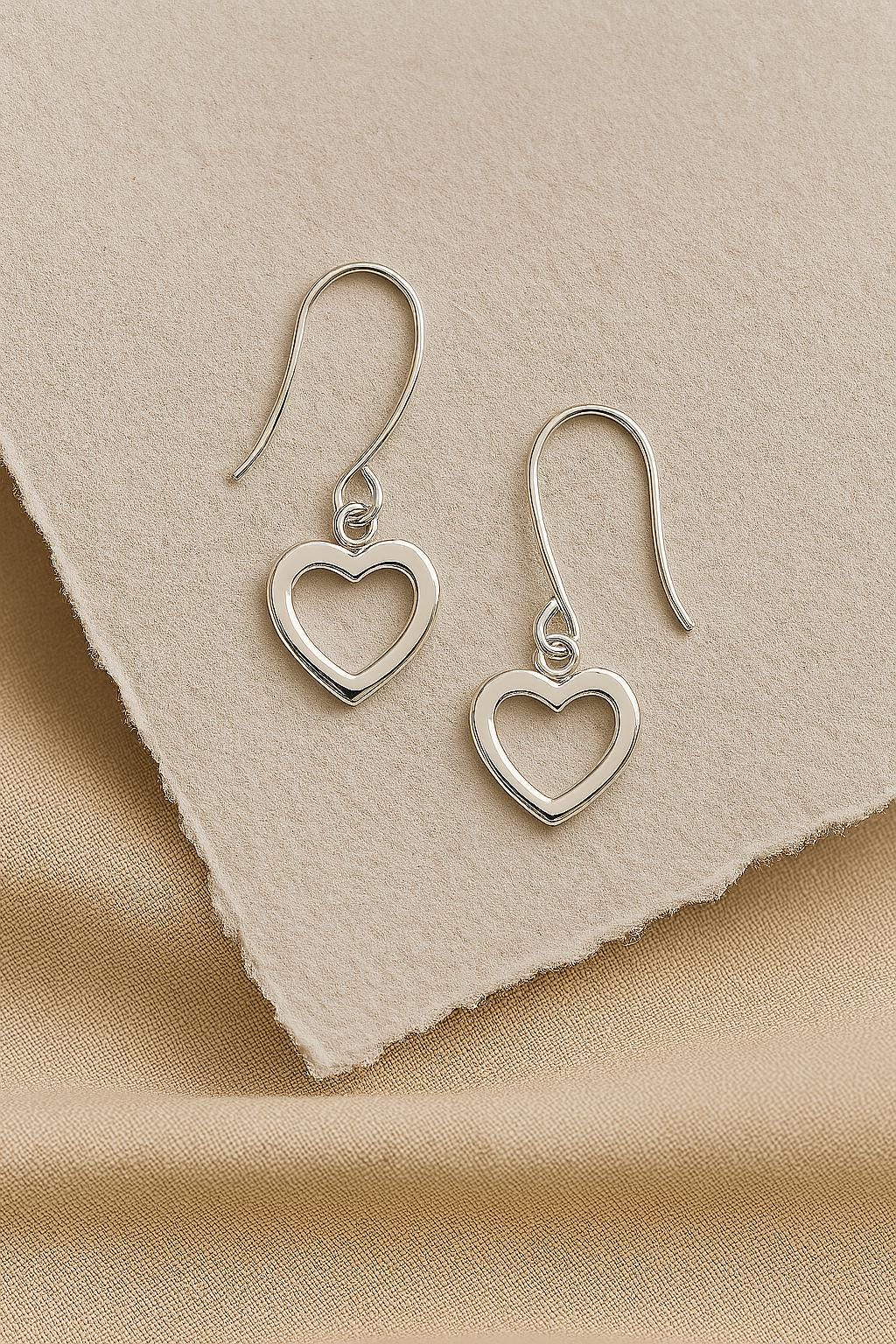 Silver heart-shaped earrings on a beige fabric background