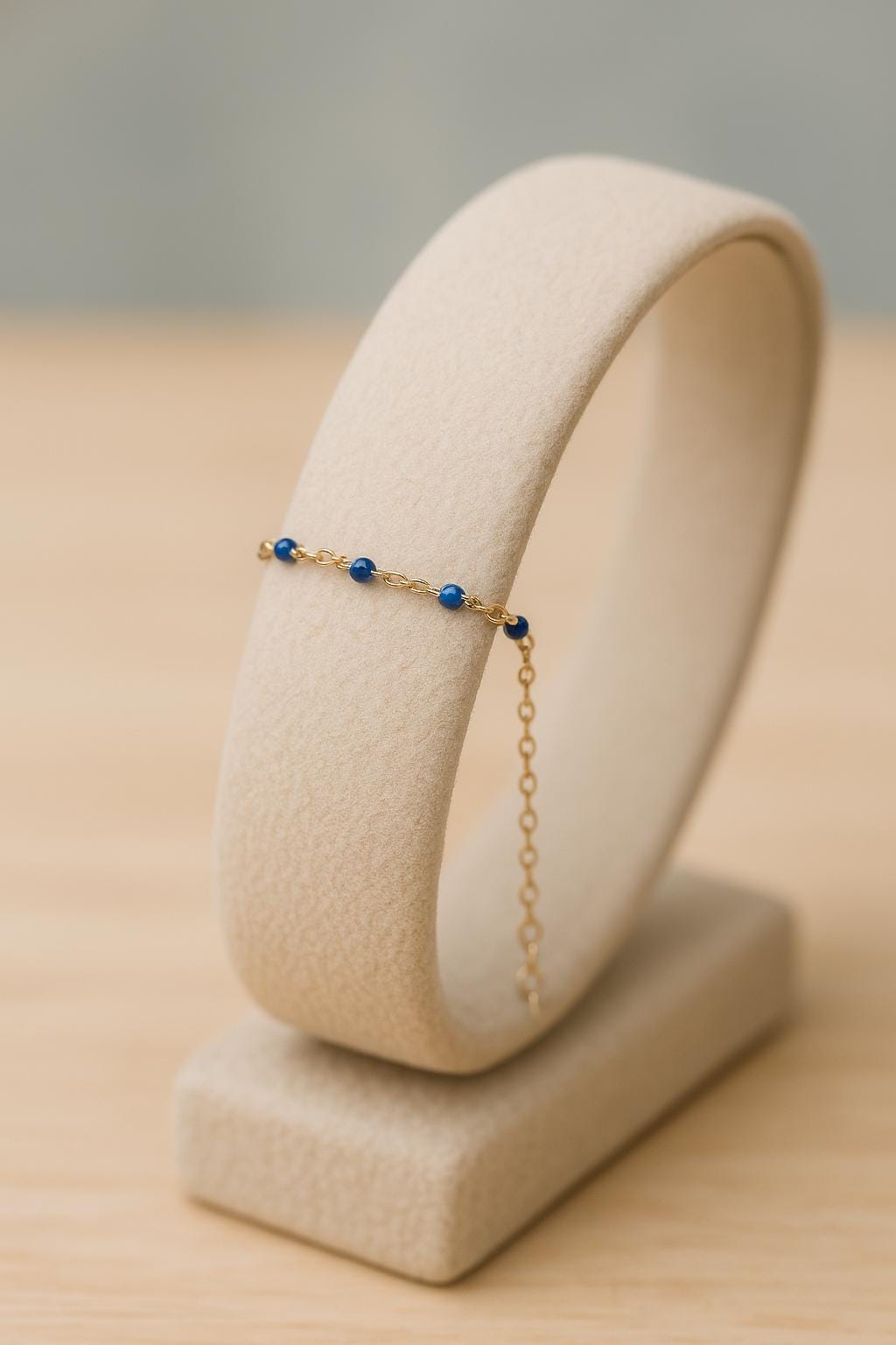 Delicate bracelet with blue beads on a beige stand against a neutral background