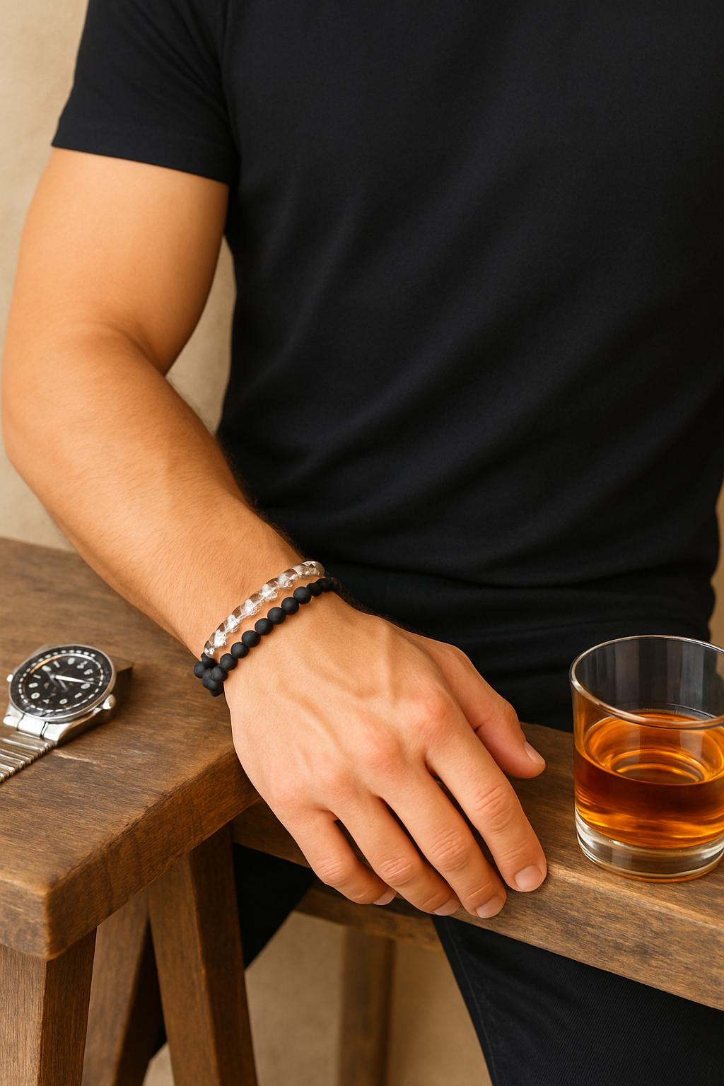 Person holding a glass of amber liquid with a watch and bracelets on a wooden surface