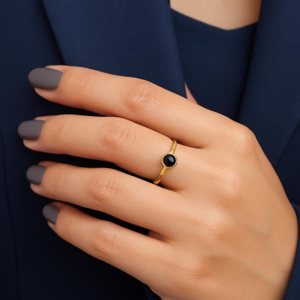 Hand wearing a gold ring with a black gemstone against a dark background
