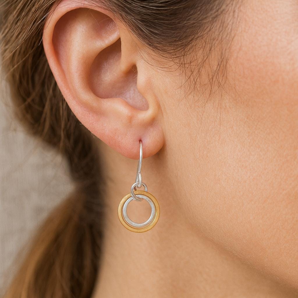 Close-up of an ear wearing a gold and silver earring against a neutral background