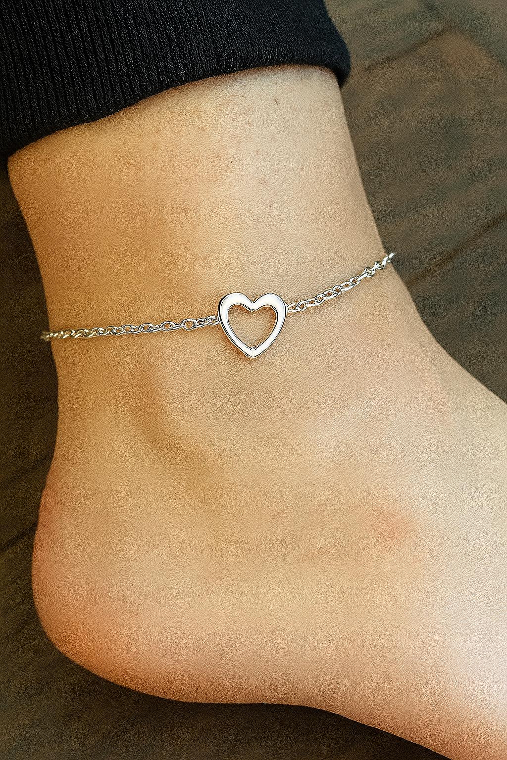 Silver heart-shaped anklet on a person's ankle against a wooden background