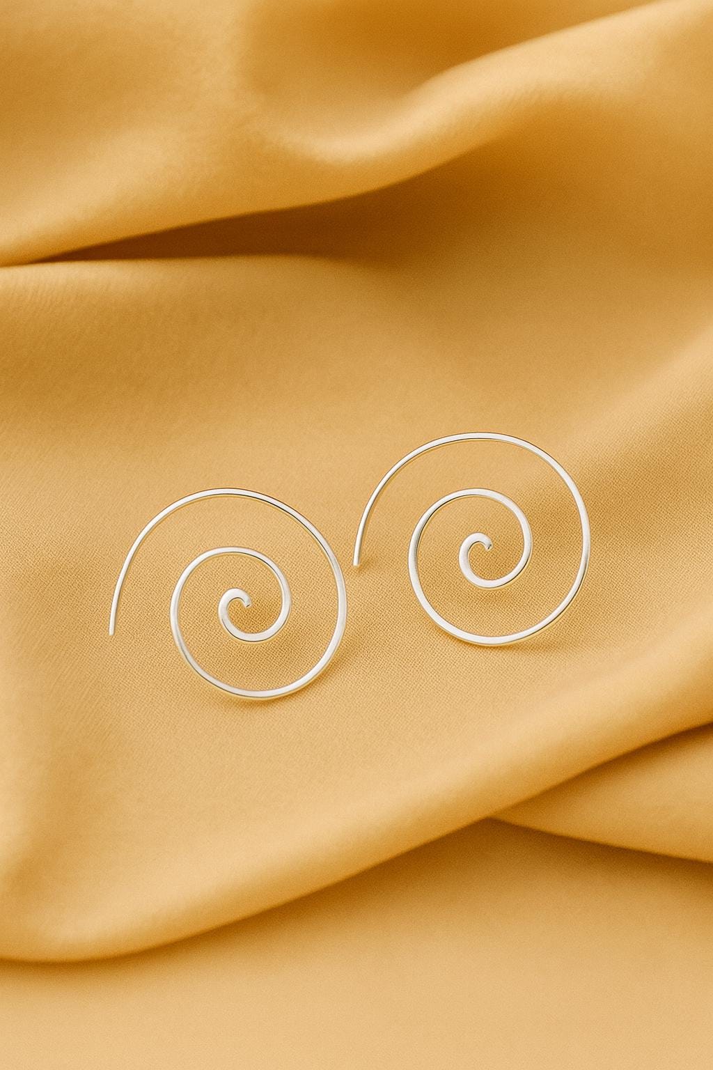 Silver spiral earrings on a mustard yellow fabric background