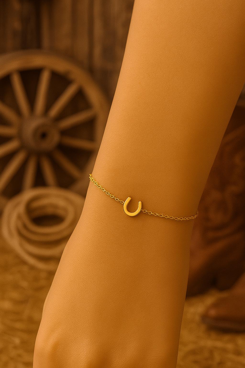 Gold bracelet with a horseshoe charm on a person's wrist against a wooden background.
