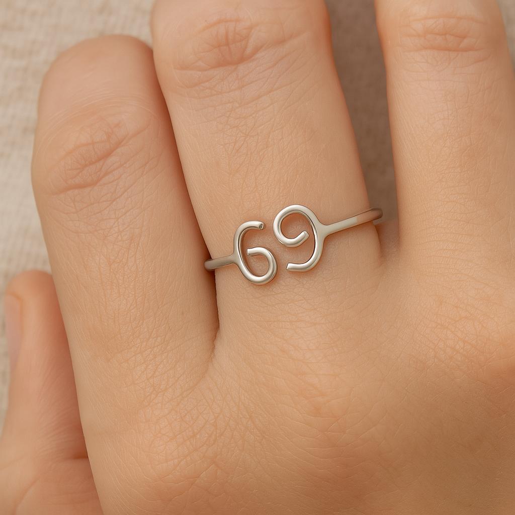 Silver ring with the number '69' on a person's finger against a neutral background