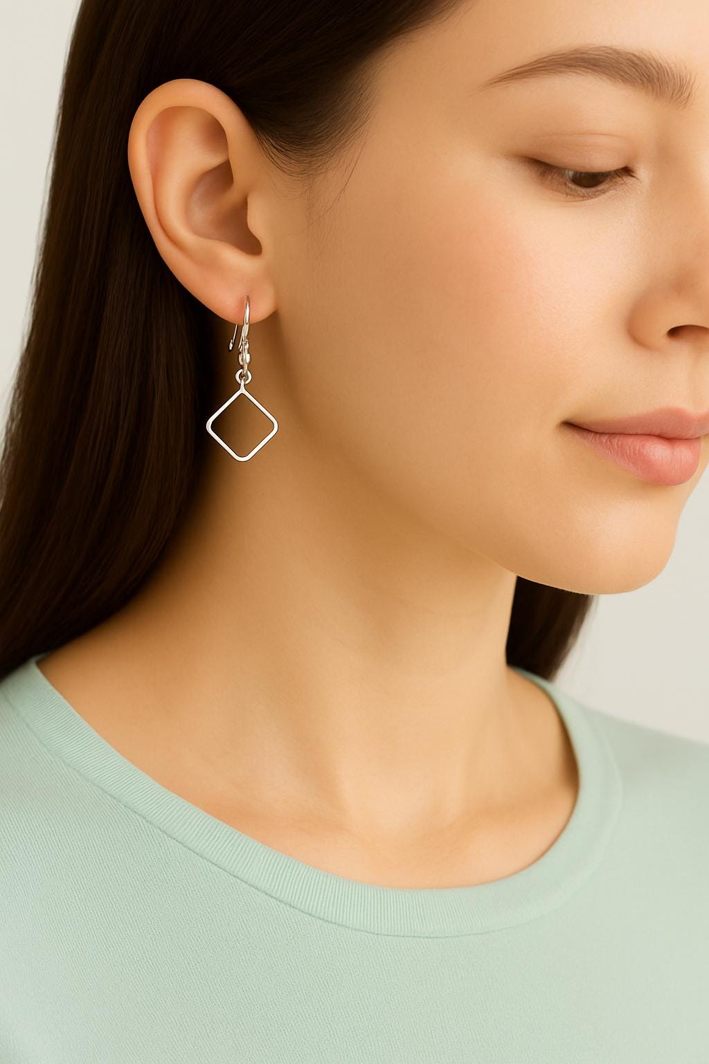 Close-up of a person wearing silver geometric earrings with a plain background