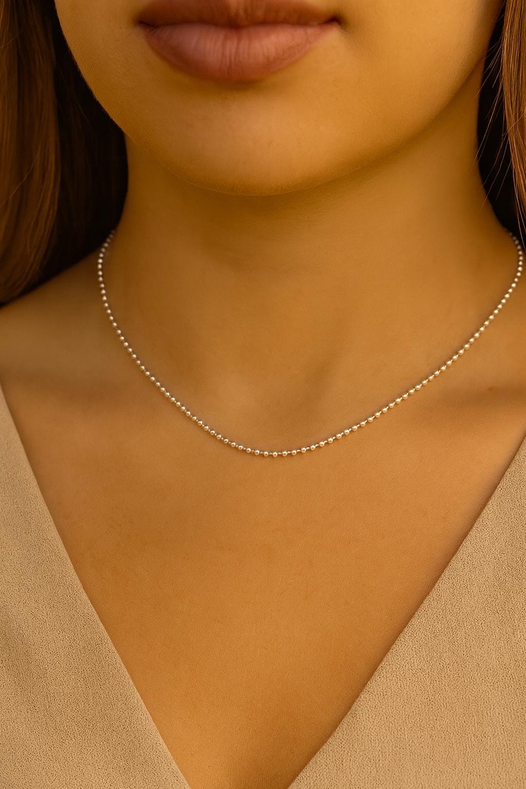 Close-up of a person wearing a delicate necklace with a neutral background