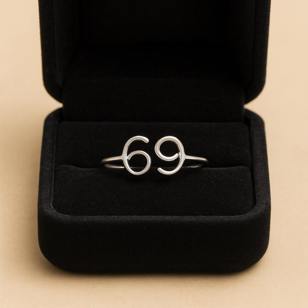Silver ring with the number '69' in a black jewelry box on a beige background