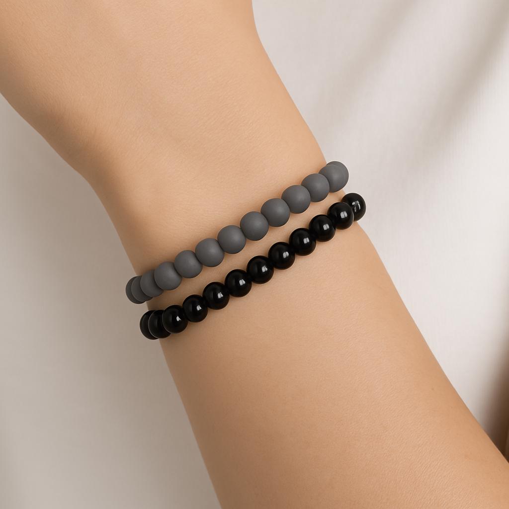 Two beaded bracelets, one gray and one black, on a wrist against a neutral background.