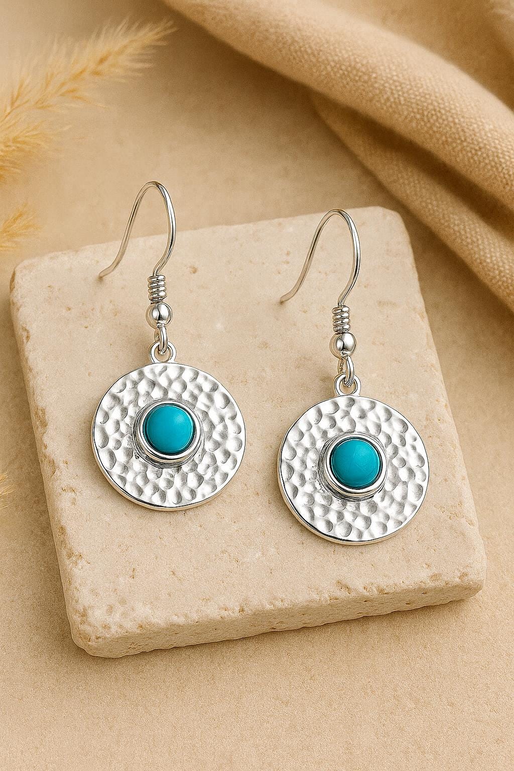 Silver earrings with turquoise stones on a beige stone surface