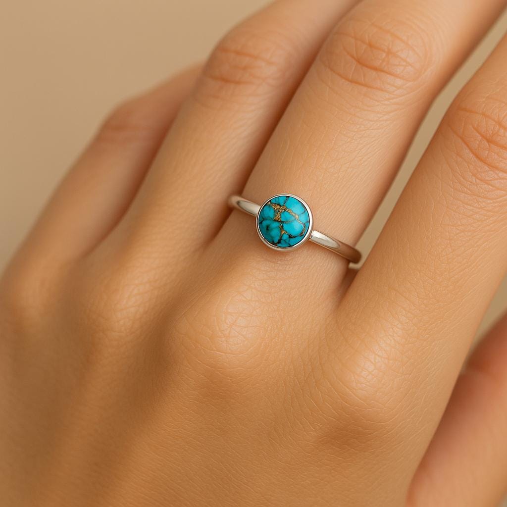 Silver ring with a turquoise stone on a hand against a beige background