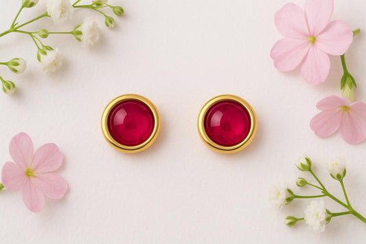 Gold earrings with red ruby gemstones surrounded by pink and white flowers on a light background