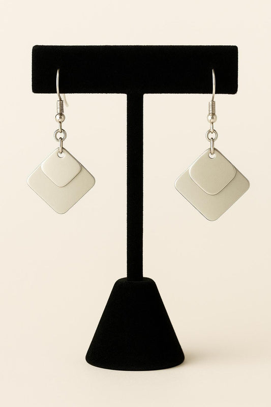 Pair of square-shaped earrings on a black earring stand against a beige background