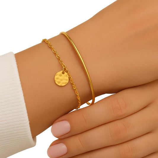 Gold bracelet with a round pendant on a wrist against a white background