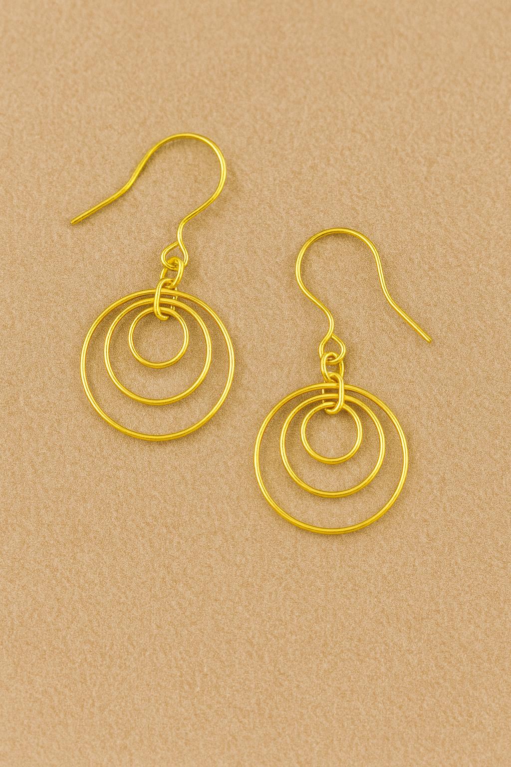 Gold Brass Dangle earrings on a textured surface with a black box in the background