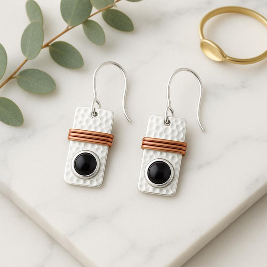Pair of earrings with black centers and brown bands on a marble surface with green leaves.