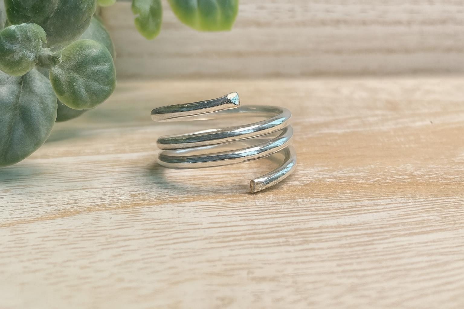 Silver spiral ring on a wooden surface with green leaves in the background