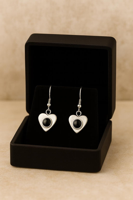 Heart-shaped earrings with black onyx gemstones in a black jewelry box on a beige background
