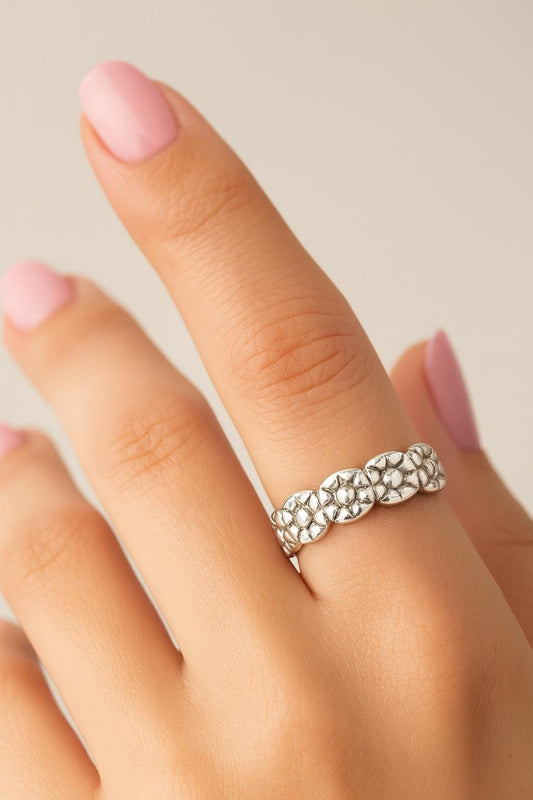 Silver floral ring on a finger with a neutral background