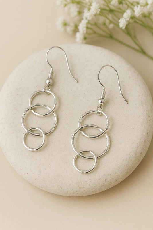 Silver chain earrings on a stone with small white flowers in the background