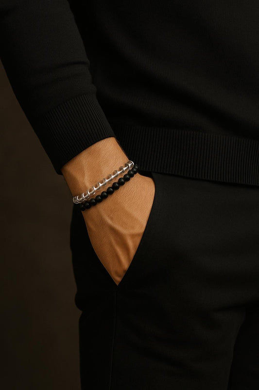 Person wearing a black sweater with a brown pocket and bracelets on a dark background