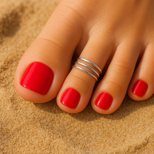 Close-up of a foot with red nail polish on a sandy background
