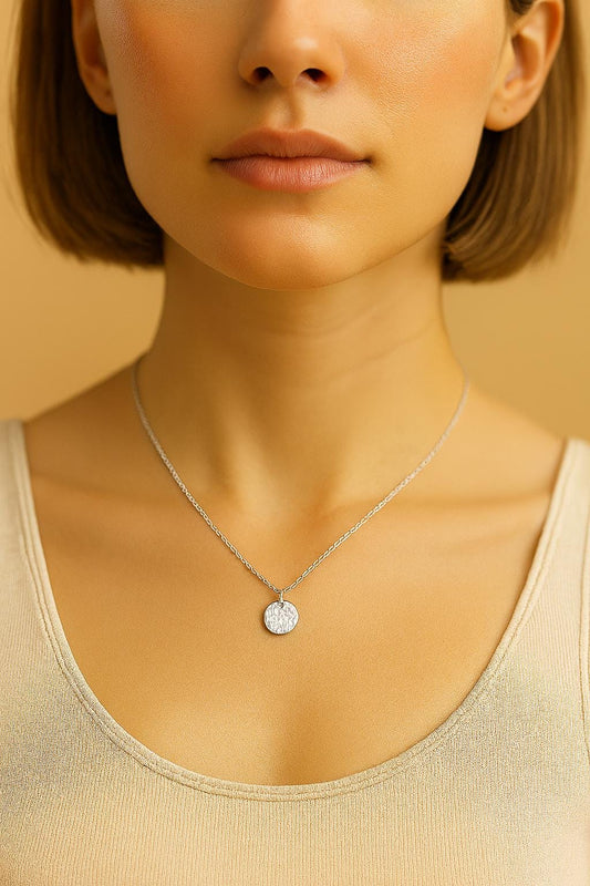 Close-up of a person wearing a silver necklace with a pendant against a neutral background