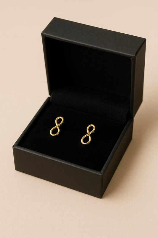 Gold infinity symbol earrings in a black jewelry box on a beige background