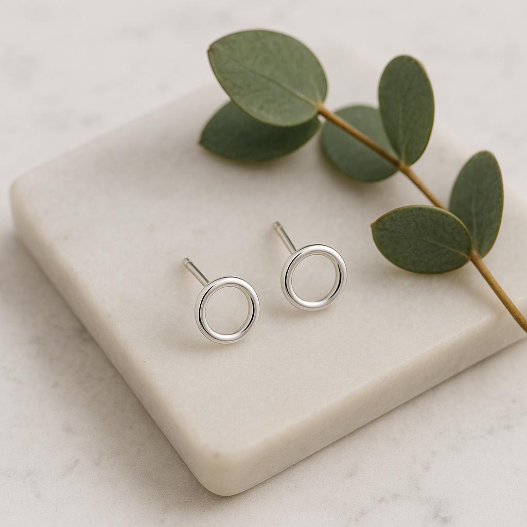 Silver circle stud earrings on a white stone surface with green leaves.