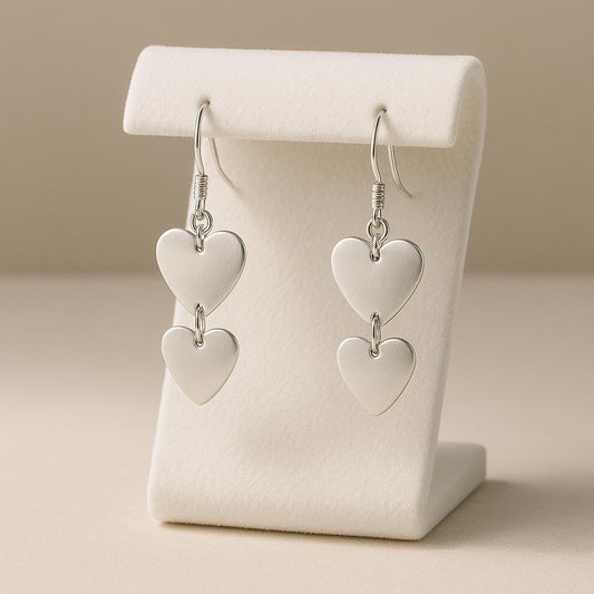 Heart-shaped silver earrings on a white stand against a beige background