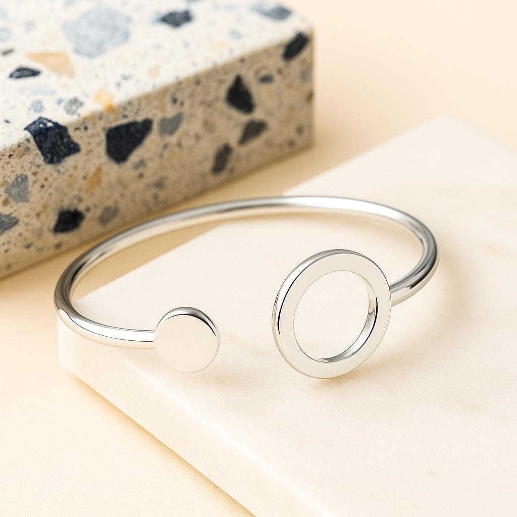 Silver bracelet on a light wooden surface with a speckled stone block in the background