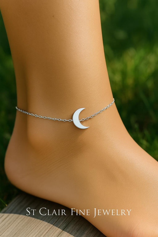 Silver crescent moon anklet on a person's ankle with a blurred green background