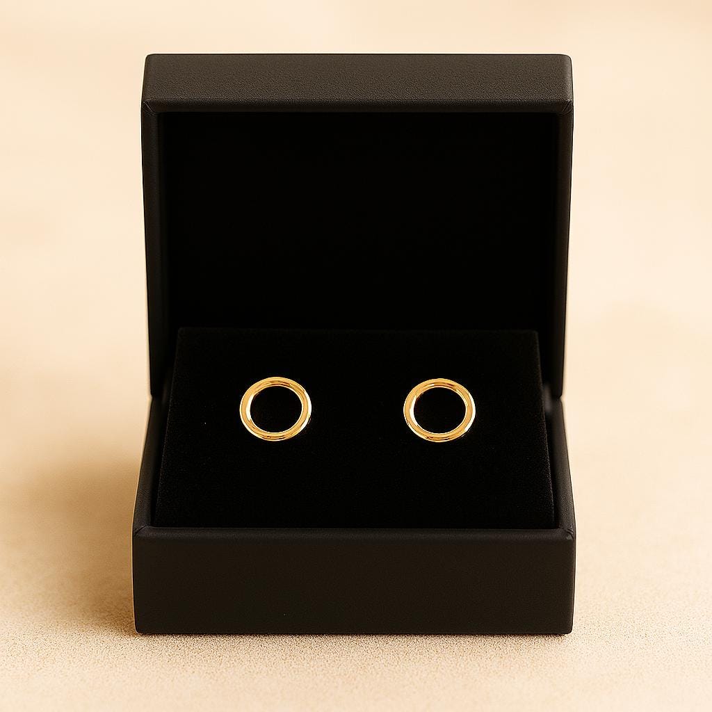 Gold earrings in an open black jewelry box on a beige background