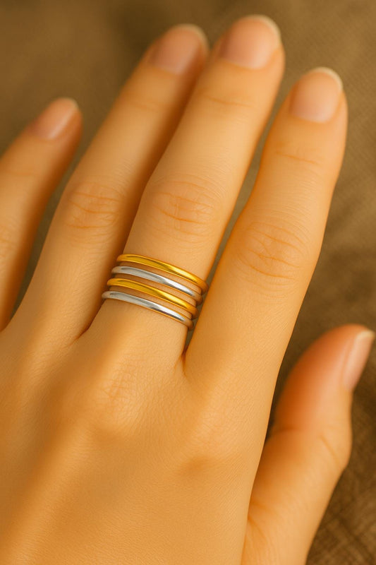 Hand wearing mix metal gold and silver rings on a neutral background