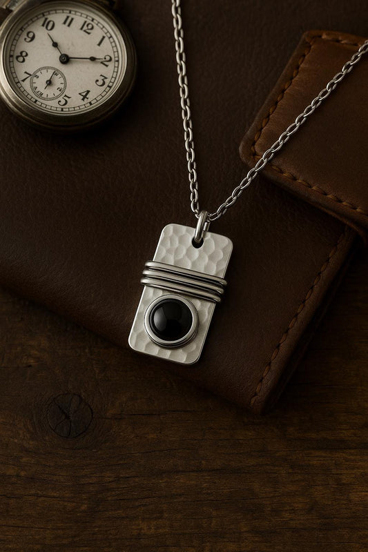 Silver pendant with black stone on a chain, placed on a brown leather surface.