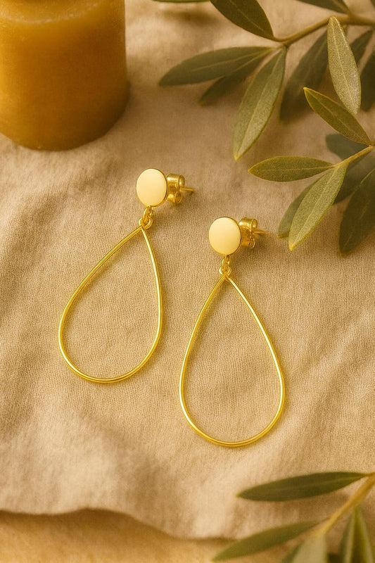 Gold earrings with white beads on a beige fabric background with green leaves.