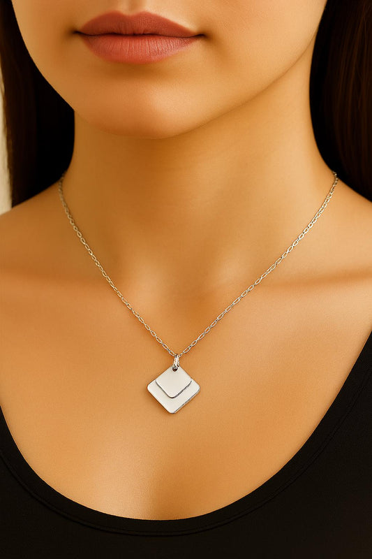 Silver necklace with a square pendant on a person wearing a black top.