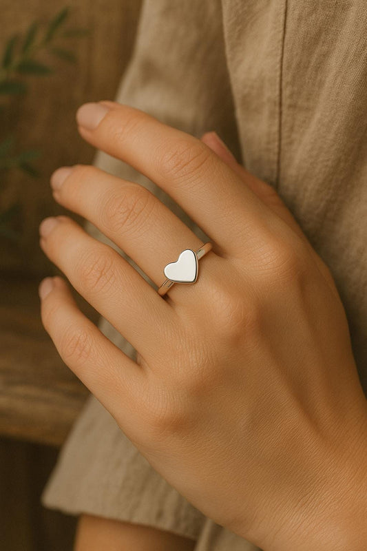 Hand wearing a silver heart-shaped ring with a blurred background