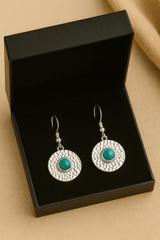 Silver earrings with turquoise stones in a black box on a beige background