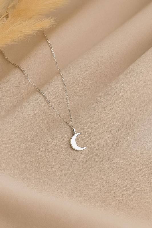 Silver crescent moon necklace on a beige fabric background