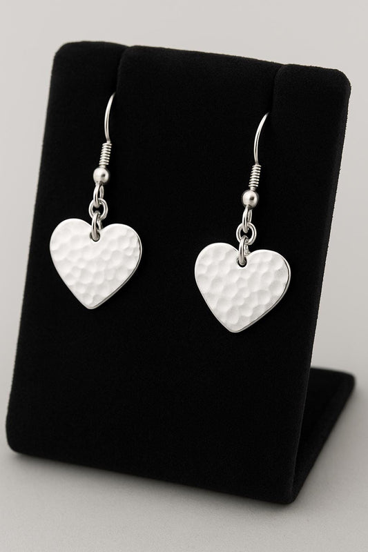 Heart-shaped silver earrings on a black earring stand.