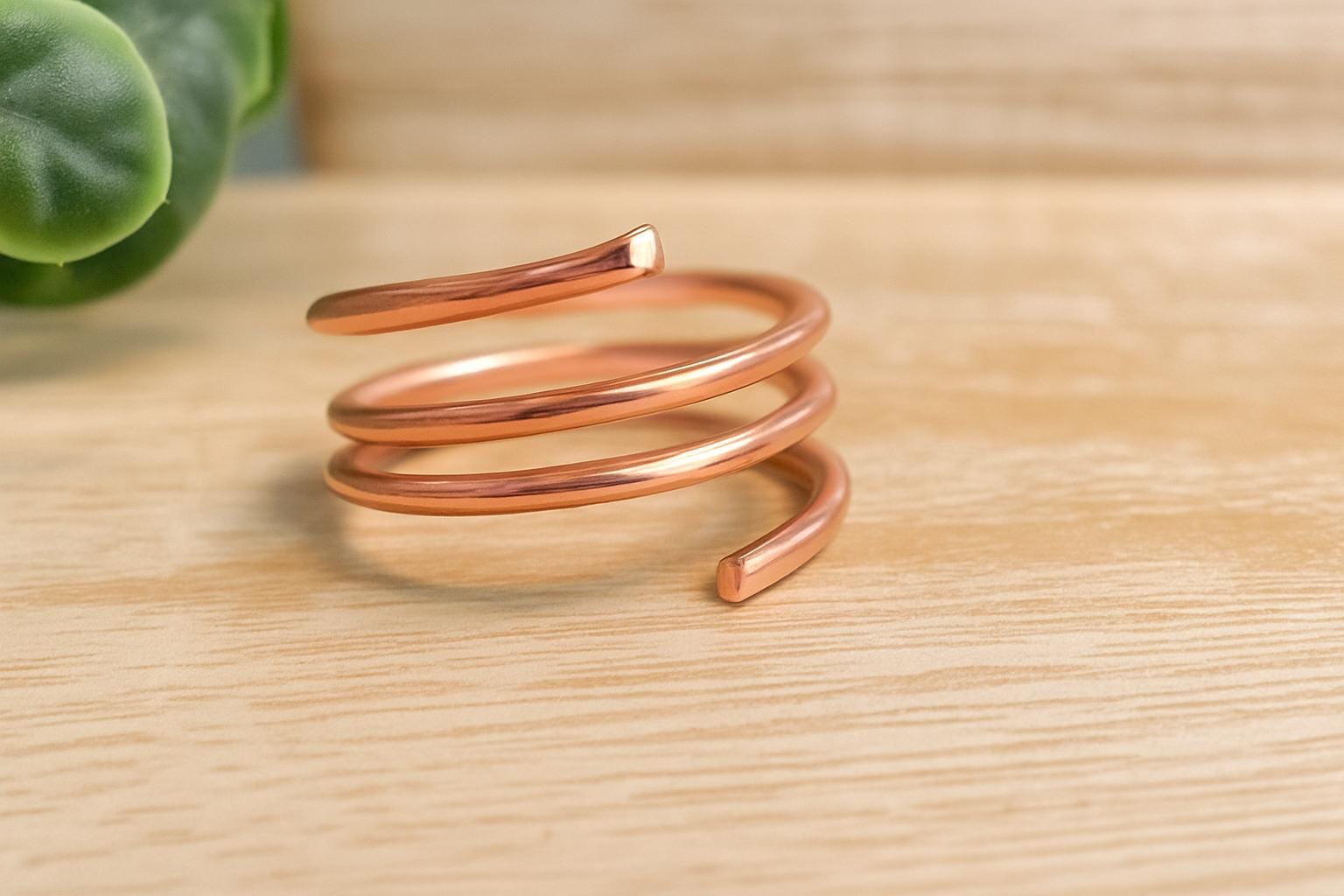 Rose gold spiral ring on a wooden surface with a blurred plant in the background